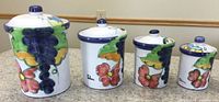 Set of four handpainted Celina canisters with lids, varying sizes from tallest to shortest, placed on beige countertop.