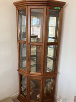 Front corner view of the wooden curio cabinet showing its height, wood finish, glass doors and sides, and overall design