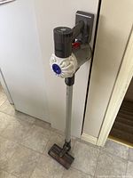 Full assembly of Dyson stick vacuum mounted on wall dock showing extension wand and motorized floor head