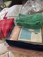 Photo showing multiple folded linens including a red plaid throw, a green throw sealed in plastic, and packaged bedding labeled Pacific Coast.