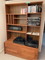Front view of wooden mid century cabinet displaying various shelves, compartments, and lower sliding door section with items on shelves (contents not included in sale).