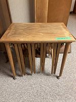 Front view of the nested tables showing four rectangular tables with tapered legs and caster wheels.