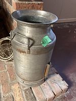 Metal milk can placed on brick near cord and against brick wall, showing side handle and body details.