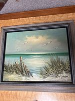 Full view of the framed oil painting showing the beach scene with seagulls and wooden fence.