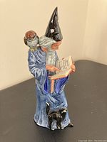 Porcelain figurine of a wizard reading a book, with an owl on his shoulder and a black cat at his feet. Blue robe and black pointed hat with star and crescent moon details.