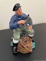 Front view of the Royal Doulton porcelain figurine The Lobster Man showing the seated man holding a lobster with a pipe in his mouth.