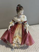 Front and side views of Royal Doulton Southern Belle porcelain figurine in burgundy and cream dress with painted floral details.