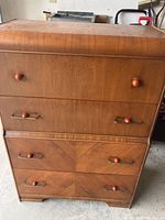 Front view of vintage wooden waterfall dresser showing four drawers with wooden handles, visible scratches and wear.