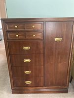 Front view of wood tall boy dresser showing six drawers and cabinet door with brass handles