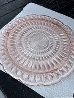 Overall view of vintage pink Depression glass plate with scalloped edge and diamond pattern on a white paper towel.