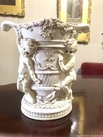 Front view of vintage cast resin vase showing two cherubs holding central urn decorated with grapevines and floral motifs, no visible damage.