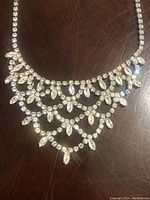 Full view of the bib necklace laying flat on a surface showing detailed rhinestone arrangement and necklace length.