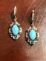 Photo showing the front view of the pair of gemstone dangle earrings with turquoise centerpiece and multicolored stones on silver filigree setting.