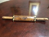 Top view of the carved wooden sheath displaying floral designs and brass mounts, placed on a wooden table.