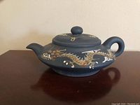 Side view of the black ceramic tea pot showing gold and white painted dragon design and rounded spout