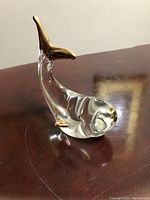 Front left angle view of the clear glass whale figurine with gold accented tail and fins showing shape and shine.