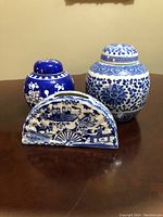 Front view of all three porcelain items on a wooden surface: two ginger jars and one fan-shaped decorative piece.