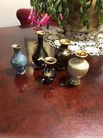 Group photo of the five cloisonné vases showing different angles and designs, placed on a wooden table with a decorative doily and a potted plant in the background.