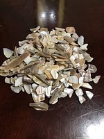 Pile of crushed abalone shells showing natural color variations and textures on a dark surface.