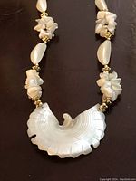 Close-up showing the large hand carved mother of pearl pendant shaped as a phoenix rising with detailed feather carving, surrounded by mother of pearl chip clusters and oval beads on the chain.