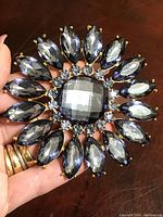 Large vintage rhinestone brooch held in hand showing faceted stones and detailing.