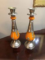 Pair of Moroccan candle holders on wooden table showing front view with orange glass and silver metal detailing.