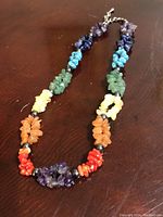 Natural stone chakra necklace laid on dark wood surface, showing full necklace with chip stones in multiple colors including purple, blue, turquoise, green, yellow, orange, and red.