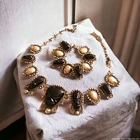 Photo showing the full necklace and bracelet displayed on a white cloth highlighting the black carved Mayan mask stones and silver bead detailing.