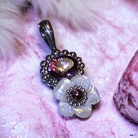 Close-up of the front side of the Sajen pendant showing the oval faceted amethyst crystal above the carved mother of pearl flower with a central garnet stone.