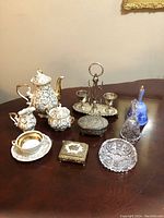 Overview of all tea time items arranged on a wooden table including porcelain tea set pieces, silver items, crystal pieces, and decorative boxes.