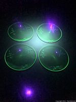 Four uranium glass plates glowing under a UV light showing characteristic green fluorescence.