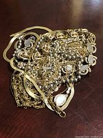 Pile of tangled gold-tone chains, showcasing variety in chain styles and some decorative elements like beads and a pendant.