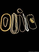 Photo showing seven pieces of vintage costume jewelry laid out on a black background. Includes five necklaces and two bracelets in gold tones and bead styles.