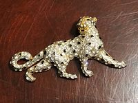 Top view of vintage tiger brooch showing gold-tone metal and rhinestone detailing on a dark wood surface.