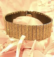 Rolled gold panel bracelet displayed coiled on a pink fabric showing textured panel design and color tone.