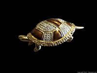 Close-up image of the turtle brooch showing gold plating, enamel sections in brown, and clusters of rhinestones on the shell.