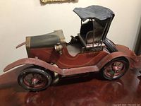 Side view of the vintage model car showing red wooden body, black fabric roof, and metal wheels.