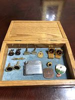 Top view of wooden box open showing cufflinks, pins, and lighter inside on blue velvet interior