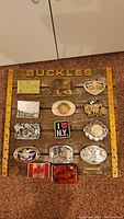 Full view of wooden display board with 14 assorted belt buckles mounted, showcasing various themes including currency print, logos, and landmarks.