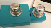 Two round ring boxes, one Birks sterling silver and one Regency plate, shown on turquoise boxes.