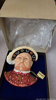 Front view of the hand painted Bossons head of Henry VIII in its box with bubble wrap inside the lid.