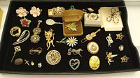 Full lot overview showing assorted brooches and earrings arranged on a black tray, with a few decorative items including a violin bookmark.