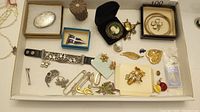 Full lot overview showing assorted brooches, heart-shaped locket, thimble, bracelet, and bangles arranged in a tray