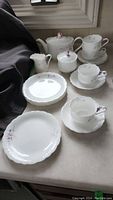 Photo of full tea set of 14 items including teapot, creamer, sugar bowl, cups, saucers, and plates displayed on counter.