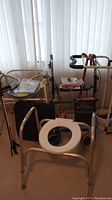 Photo showing a variety of assistive aids including the commode chair, raised toilet seat, canes, bedrail, blood pressure monitor, and walker.