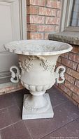 Front right angled view of large Grecian style round resin planter showing scalloped edge, floral and leaf motifs, and decorative handles.