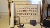 Framed vintage poster of military decorations and medals along with framed military photo and packaged figurines arranged on floor.