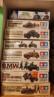 Stacked boxes showing titles and scale of military models by Tamiya and Italeri, including German tank crew and Panzerkampfwagen II tank