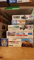 Photo of stacked model kit boxes showing the brands and model names for five military vehicles, including a Stuart tank and ambulance jeep.