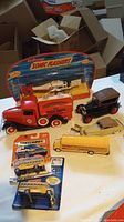 Models displayed on a table with fire truck, black vintage car, cream vintage car, coast guard helicopter in original packaging, and various school bus models